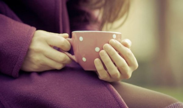 Kvinne med lilla kåpe holder en kopp