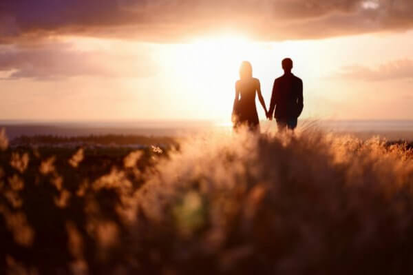 Par i en eng holder hender i solnedgangen