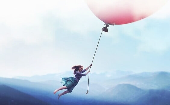 en jente som holder seg til en gigantisk ballong over fjellene