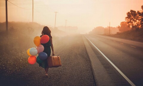 Kvinne med ballonger og koffert kan se håp i mørket