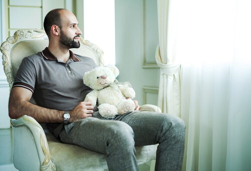 Mann som holder en bamse ser ut av vinduet