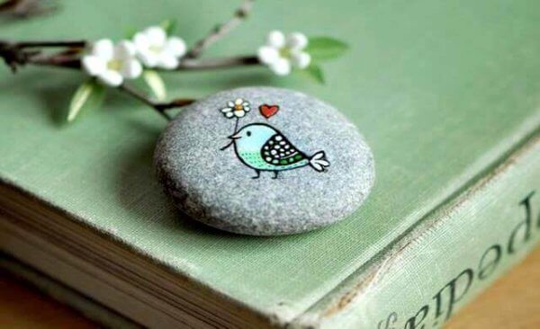 En fugl som bærer en blomst, malt på en stein.
