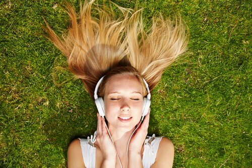 Jente ligger i gresset og lytter til musikk