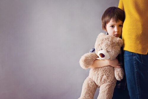 Trist gutt søker trøst hos moren og holder en bamse