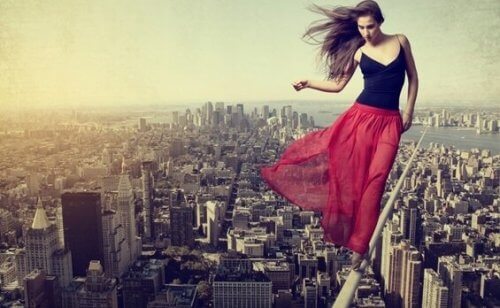 Kvinne med rødt skjørt balanserer på line over en by