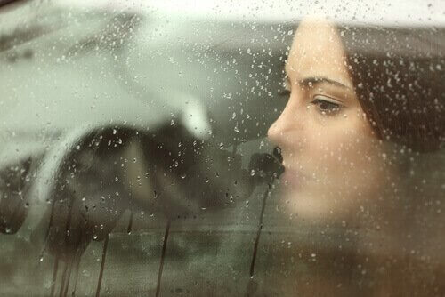 Kvinne bak vindu med regn