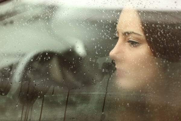 Kvinne ser ut vindu med regn
