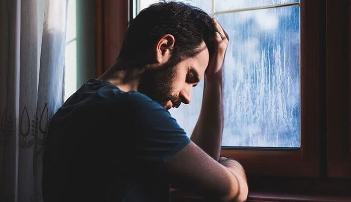 Trist mann ved et vindu lider av reaktiv depresjon