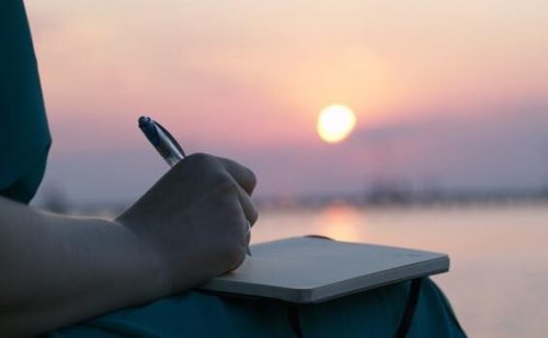 En person skriver dagbok i solnedgangen
