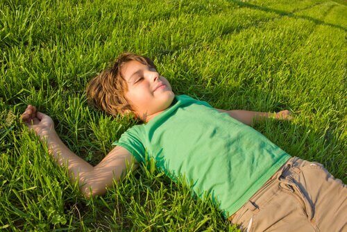 Liten gutt legger seg i gresset med et smil om munnen