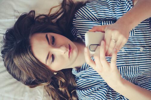 Ung jente ligger på en seng og sjekke sin mobiltelefon, er sosiale medier en del av moderne tvangslidelser