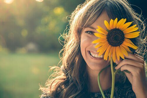 Smilende kvinne holder opp en solsikke