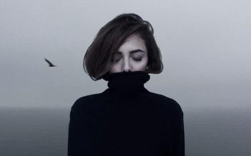 EnIntroversjon med høy-fungerende angst? Bilde av en ung kvinne som lukker øynene og gjemmer seg i en svart høyhalser