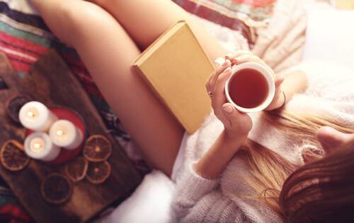 Kvinne sitter med en bok og en kopp te i hånden