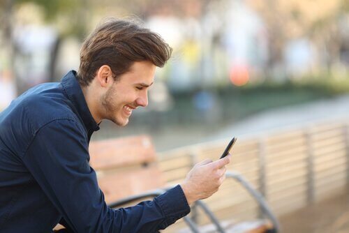 Mann driver med nettdating og smiler mot telefon
