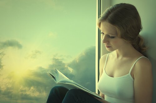 Jente leser bok ved vinduet.