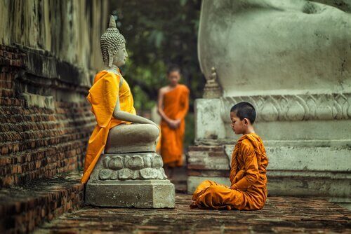 En gutt som sitter foran en statue av Buddha og praktiserer en type av buddhisme