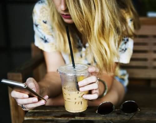 En kvinne på telefonen mens hun drikker is-kaffe.
