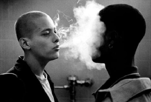 Hvit mann blåser røyk i ansiktet på svart mann.