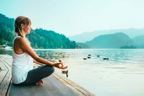 Ung kvinne mediterer på en brygge ved en innsjø
