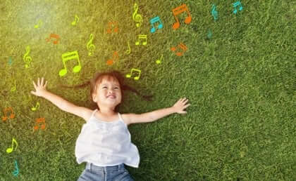 Glad jente ligger i gresset og lytter til musikk