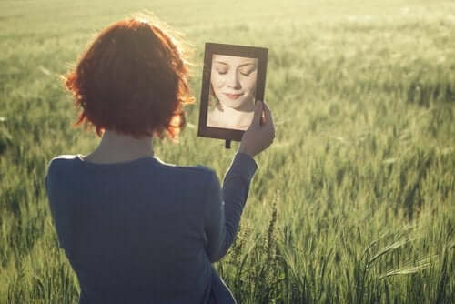 En rødhåret kvinne holder opp et speil forran sitt eget ansikt samtidig som hun lukker øynene.