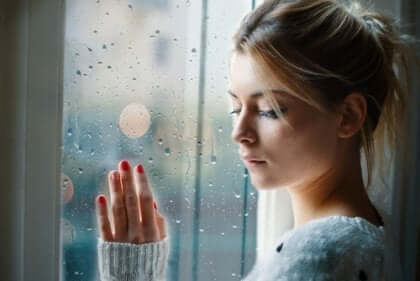 Trist kvinne med hånden på et vindu