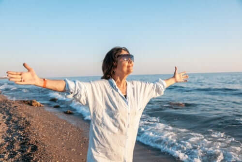 En eldre kvinne som står på en strand med armene spredt bredt.
