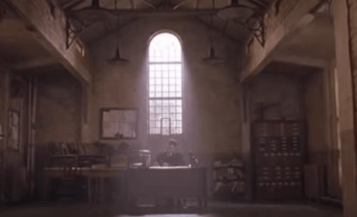 En mann som sitter ved et skrivebord i et muggent rom i et fengsel.