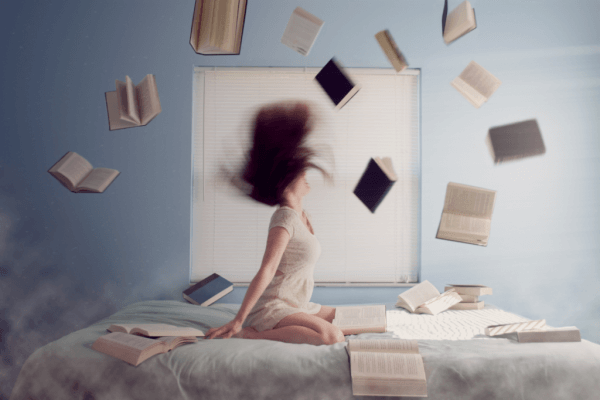 Kvinne på senga med flyvende bøker