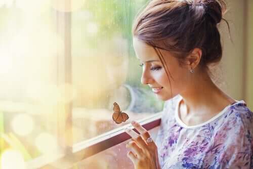 En kvinne som smiler til en sommerfugl på vinduet.