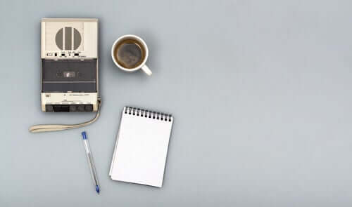 En opptaker ved siden av en kopp kaffe, en notatbok og en penn.