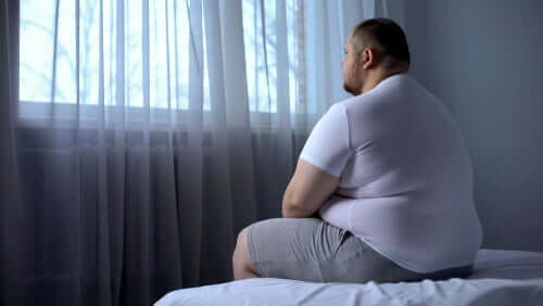 En overvektig mann som sitter på en seng.
