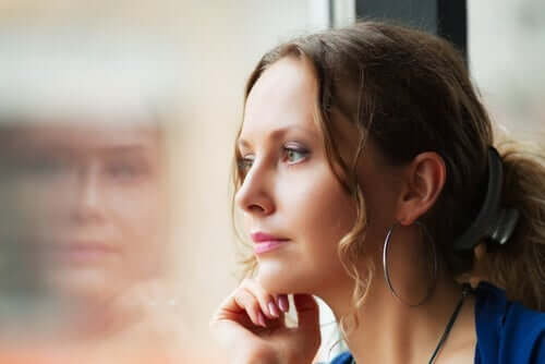 Kvinne ser ut av vindu og på sitt eget speilbilde