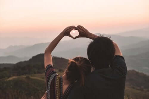 Mann og kvinner former hendene til et hjerte forran solnedgang.