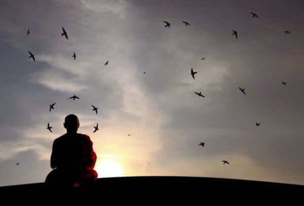 munk mediterer forran en kveldshimmel full av fugler