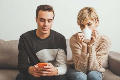 En kvinne som ser på kjærestens mobiltelefon mens hun drikker kaffe