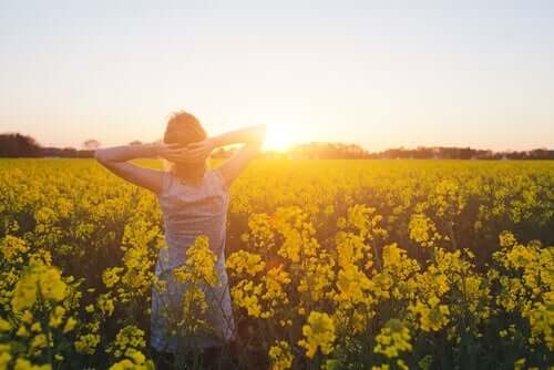 En kvinne står midt i en eng full av gule blomster i solnedgang.