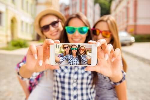 Tre smilende veninner med solbriller tar en selfie 