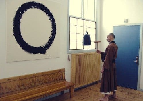 En buddhistisk munk som stirrer på ensō-sirkelen på en vegg.