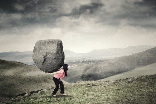 En kvinne vandrer i et fjelllandskap med en stor sten på ryggen.