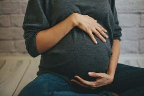 En gravid kvinne som holder seg på magen sin.