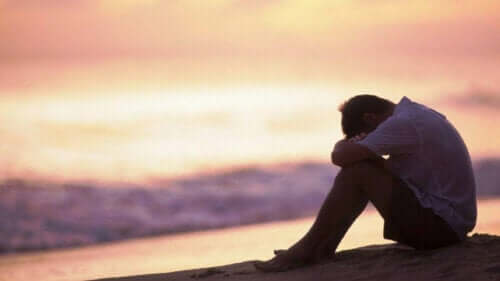 En trist mann som sitter ved stranden og tenker på ytre følelsesregulering.