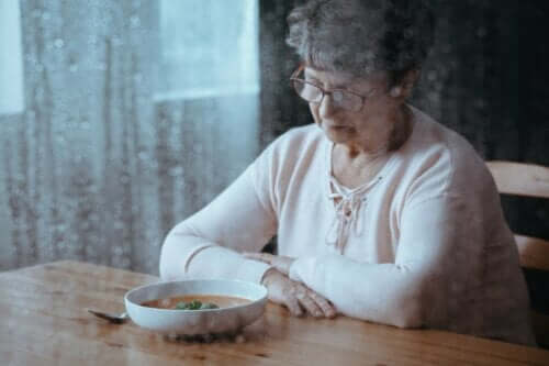 En eldre kvinne som er lei seg og ser på en tallerken med mat.