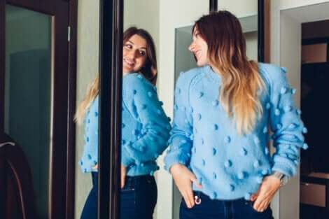 En kvinne iført genser som ser seg i speilet.