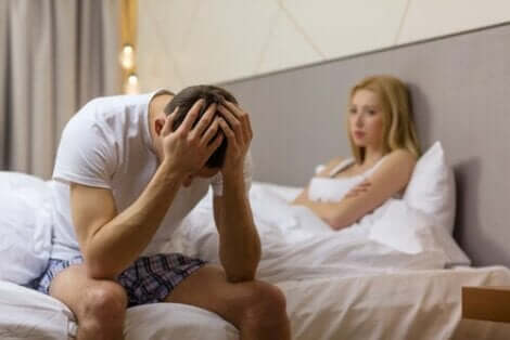 En mann som sitter på siden av en seng med hodet i hendene etter sex.