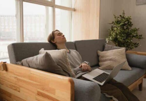 En mann som sover på sofaen med laptop på fanget.